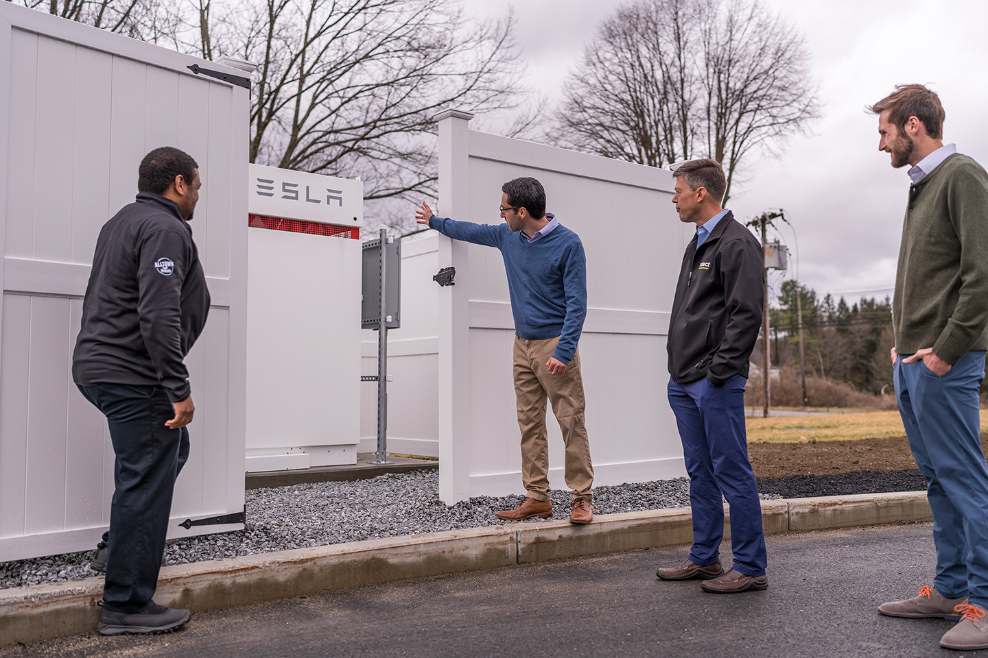 Employees view a large Tesla battery storage unit at a resilient service station in Massachusetts.